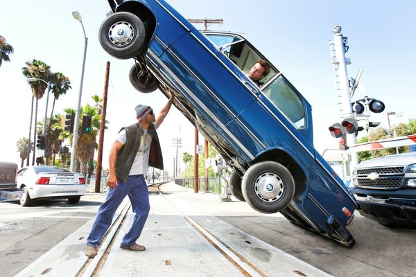 A strong man lifts a car with a driver