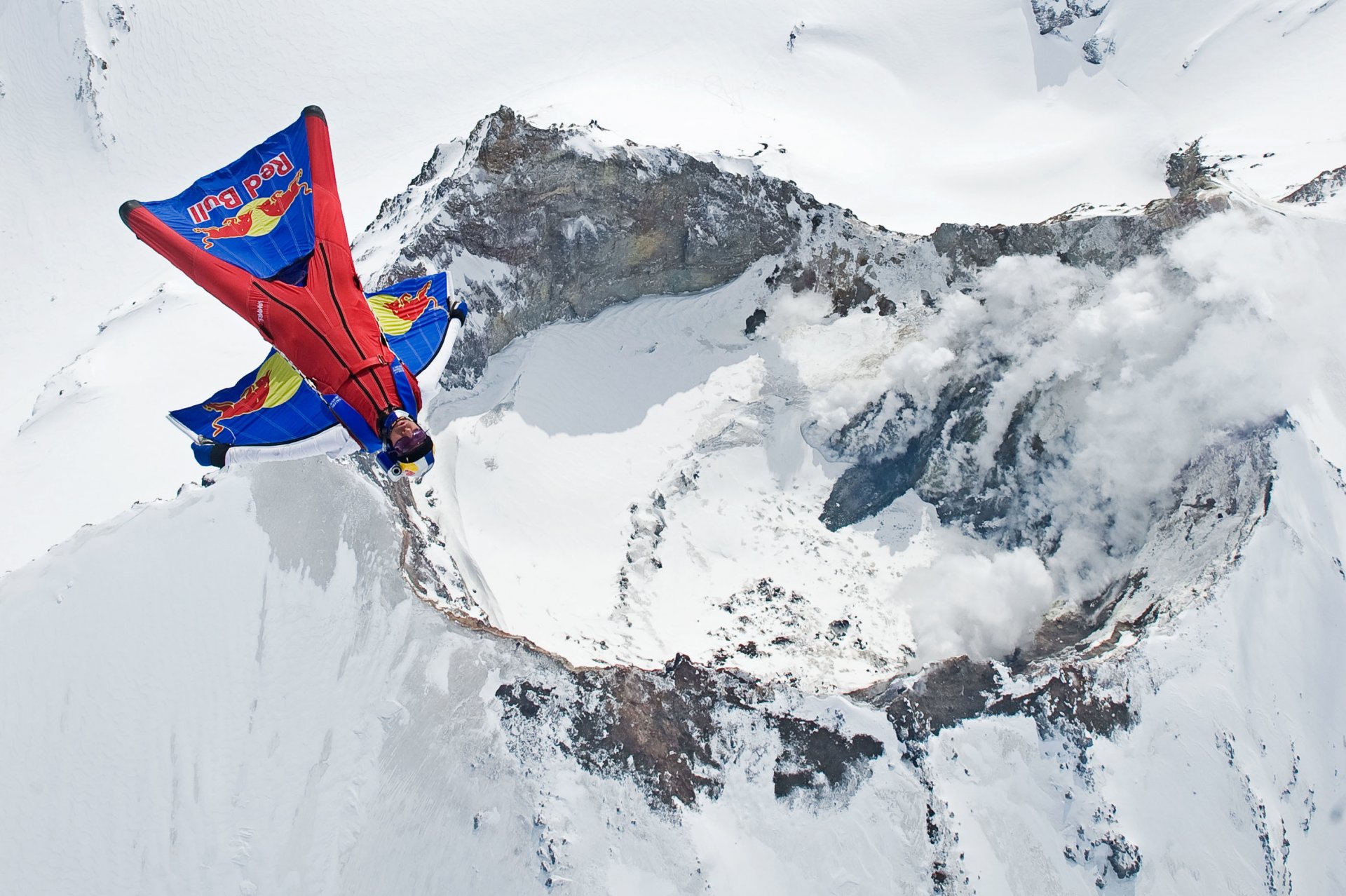 wingsuit pilot fliegen flieger vulkan berg rauch schnee winter container fallschirm roter stier extremsport