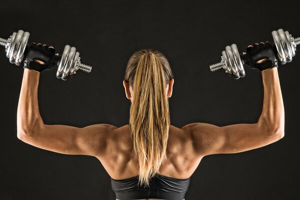 Die sportliche und muskulöse Blondine von hinten hält Hanteln