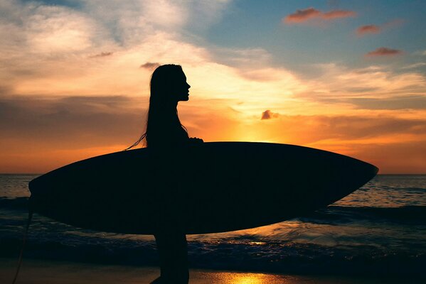 Silhouette of a girl with a surfboard against the background of the sea and a magnificent sunset