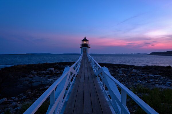 Seascape with pier and lighthouse at sunset