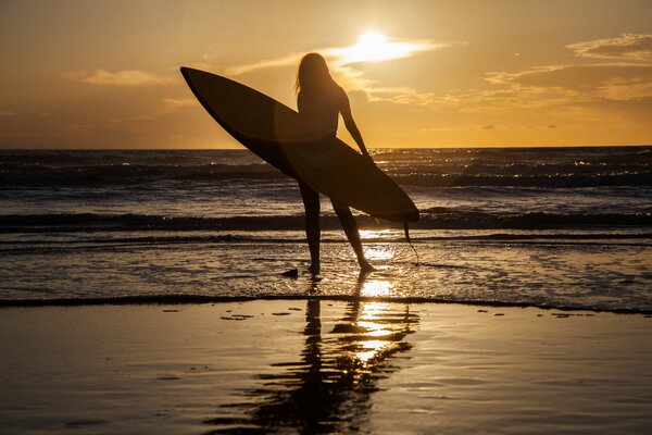 Chica de pie en la arena junto al mar con una tabla