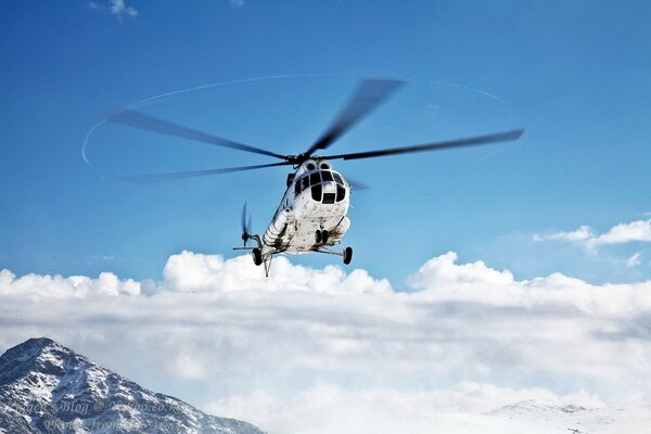 El helicóptero vuela en el aire sobre las nubes y las montañas