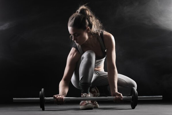 A girl in a gray leotard lifts a barbell