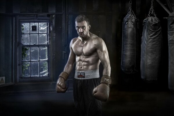 Homme gonflé avec des gants de boxe sur fond de boîte et de sacs de boxe