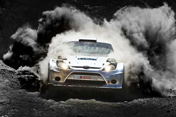 A sports car drives along a black road, dispersing dust