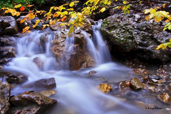 Kleiner steiniger Wasserfall im Herbst