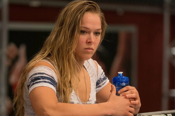 Chest photo of American wrestler Ronda Rousey in a white T-shirt, with a blue water bottle in her hands