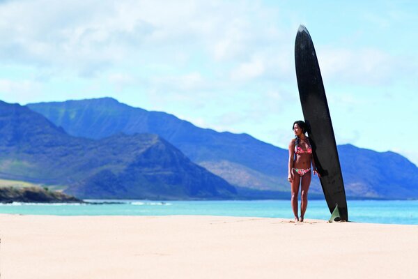 A girl in a swimsuit is a surfer on the beach