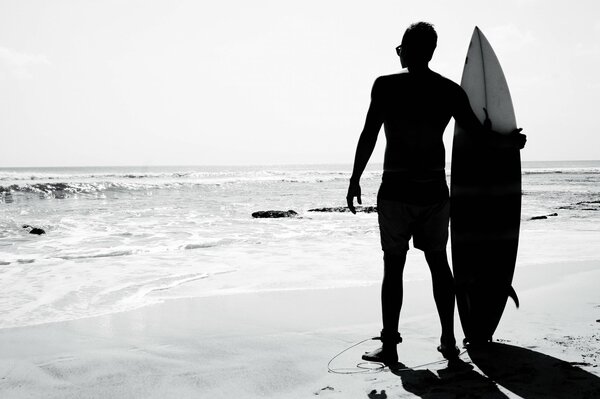 Foto in bianco e nero del surfista con la tavola sulla spiaggia