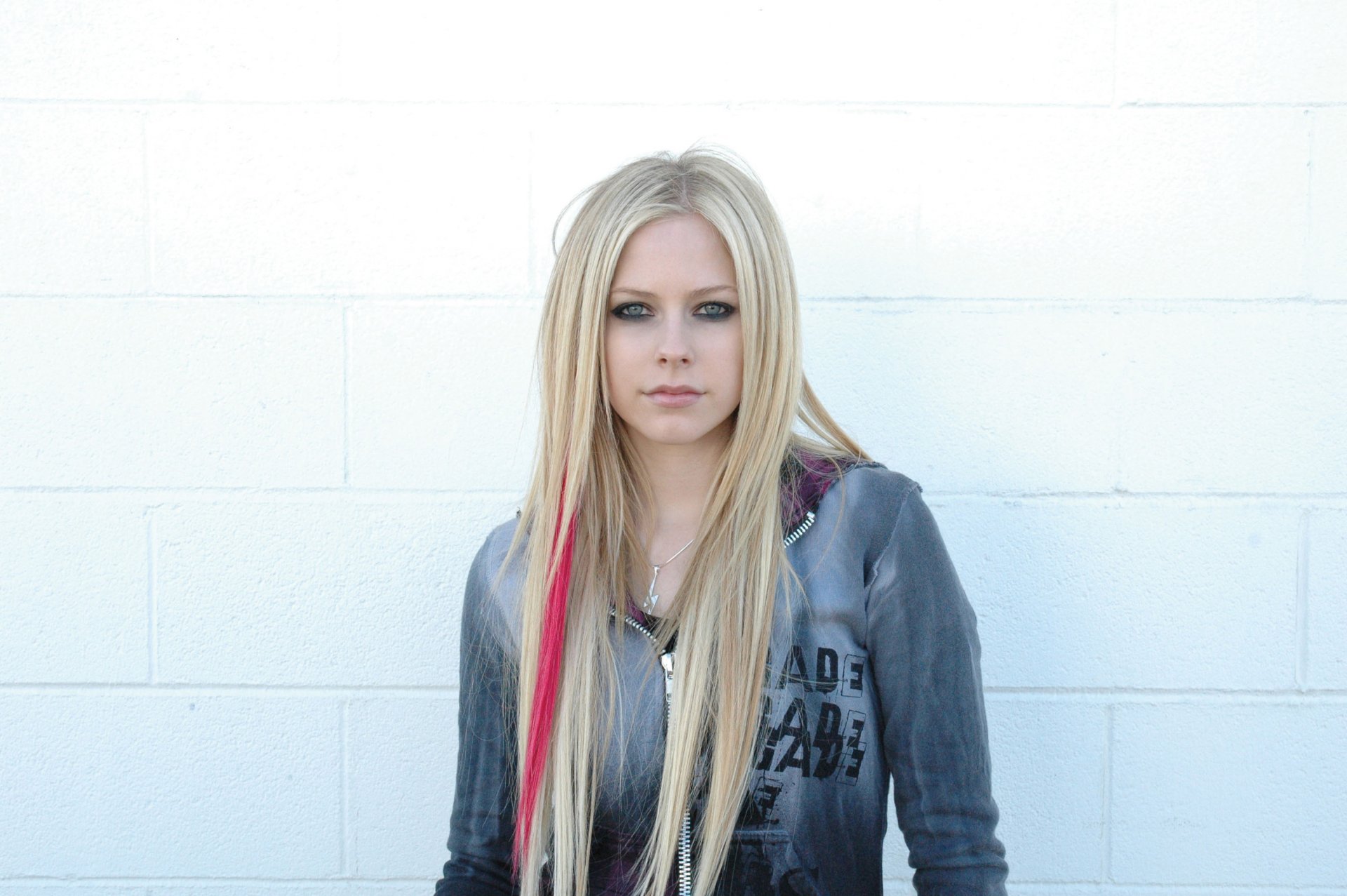 ragazza avril lavigne famosa cantante rock in piedi sopra un muro bianco guardando la telecamera striscia tra i capelli