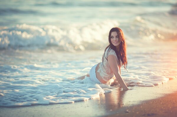 Chica en camiseta mojada en la playa en el agua