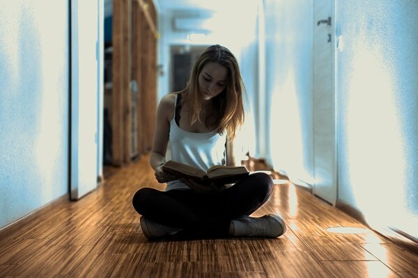 The girl is sitting on the floor in the corridor and reading a book