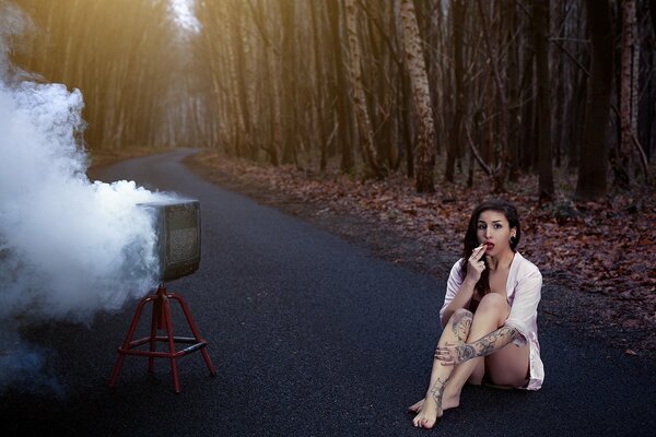 A young girl in a shirt is sitting on the road in the forest