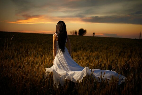 Fille en robe blanche dans le champ au coucher du soleil