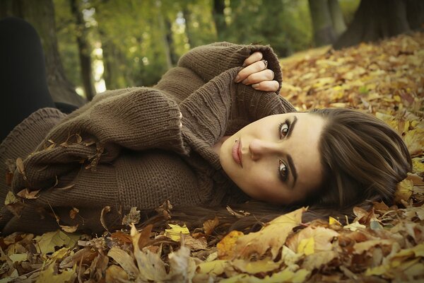 Fille en pull posant dans les feuilles