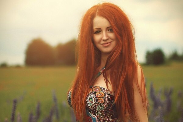 Belle fille aux longs cheveux roux, avec un sourire chic, sur fond de champ