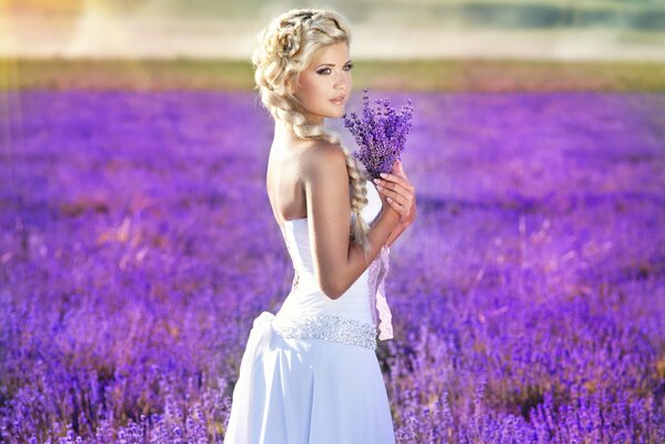 Belle fille en robe blanche se trouve dans un champ avec un bouquet de lavande dans les mains