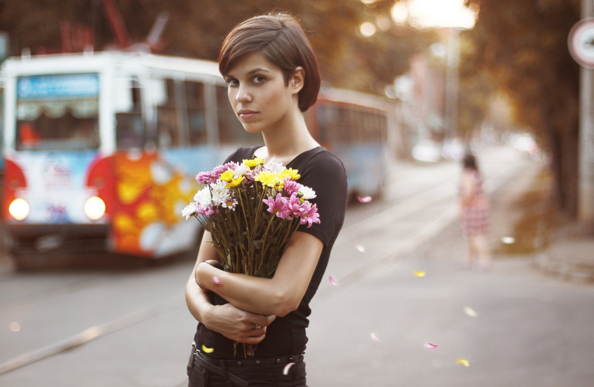 chica ramo flores pelo castaño ojos marrones vista tranvía ciudad pétalos