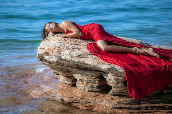 A girl in a red dress on a rock against the background of the sea