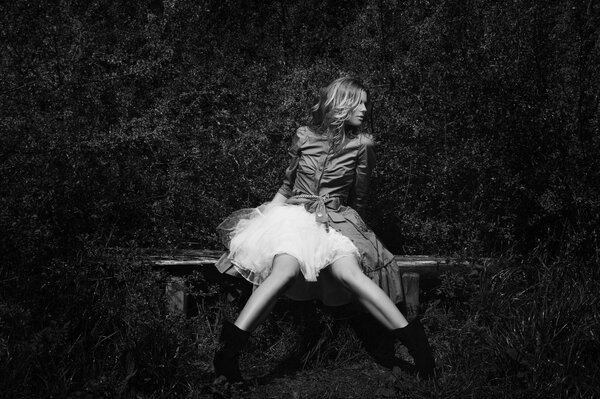 Foto en blanco y negro de una niña en un banco con un vestido blanco