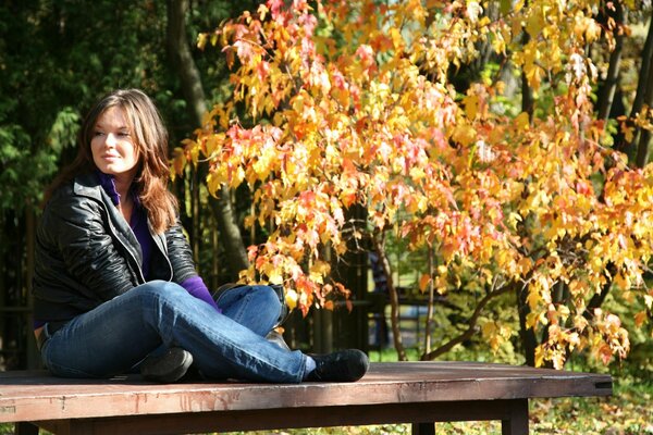 A girl is sitting on a bench in autumn