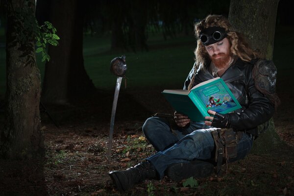 A long-haired man with a beard reads a book of fairy tales in the forest