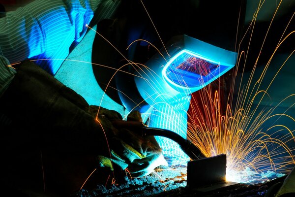 A welder in a helmet at work. Sparks from welding