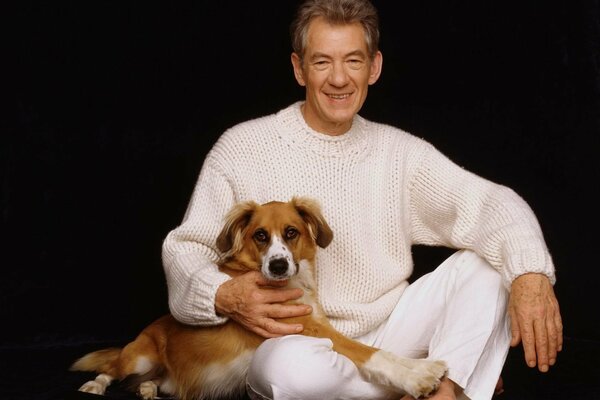 An elderly man in white is sitting with a dog