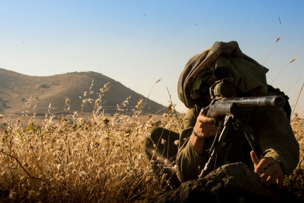 A sniper with a rifle is sitting in ambush