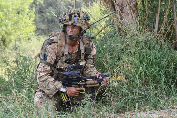 Ein Soldat in Tarnung versteckt sich mit einer Waffe in einem Gebüsch