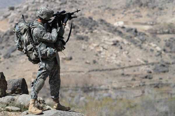 A soldier with a gun stands on a rocky shore