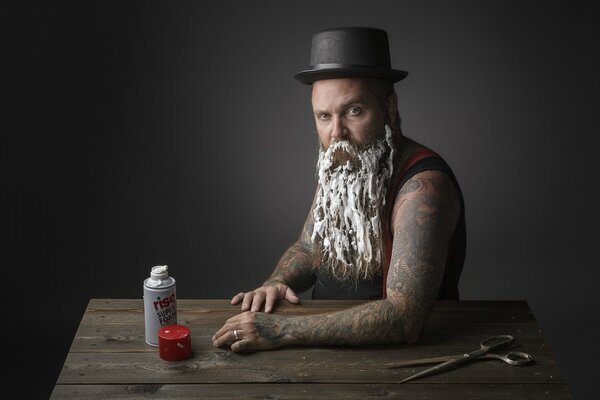 A man with a hat and tattoos smeared foam on his long beard