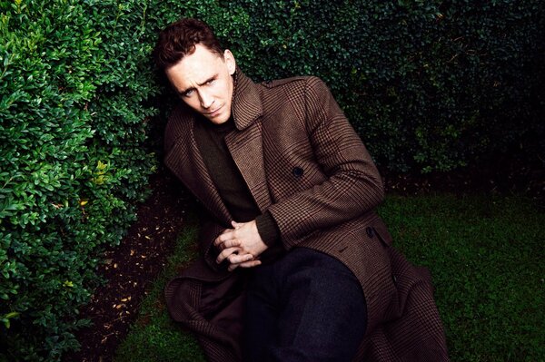 Tom Hiddleston is lying on the grass in the bushes