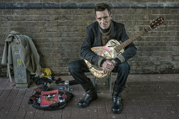 El hombre con la guitarra en la pared de ladrillo