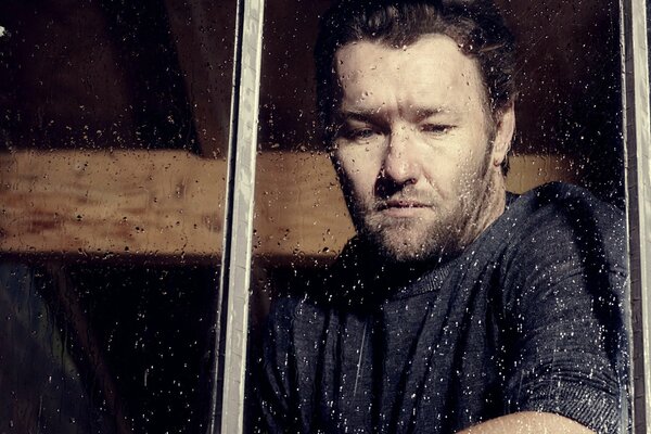 El melancólico y triste Joel Edgerton junto a la ventana con gotas de lluvia