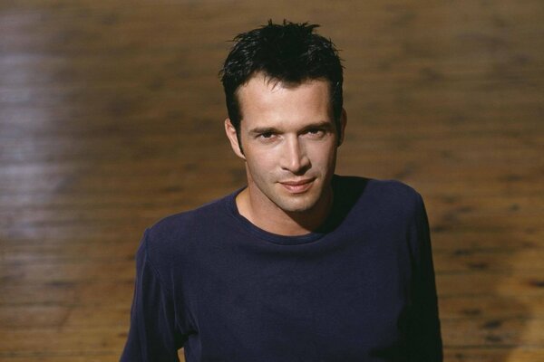 Actor James Purefoy, sitting on the parquet floor, looks piercingly into the camera