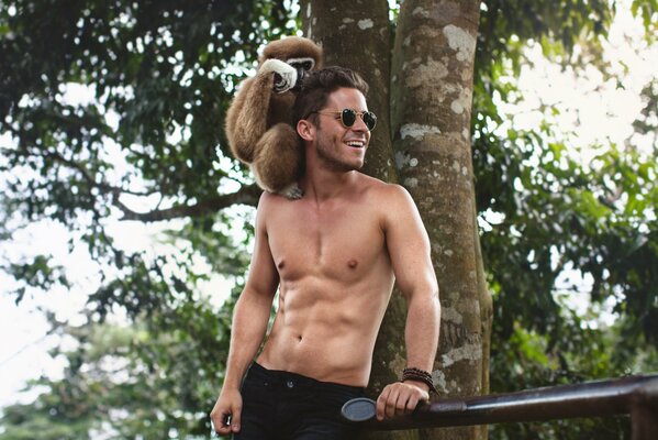 A guy with a naked torso has a monkey sitting on his shoulder