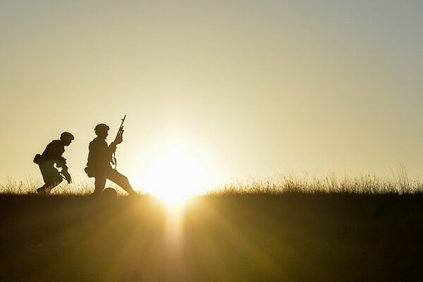 Silhouettes of soldiers with weapons in their hands at sunset