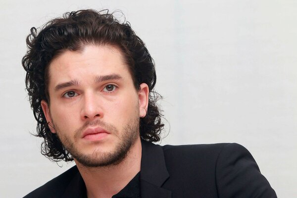 Actor Keith Harington on a light background in a black suit looks sadly into the distance