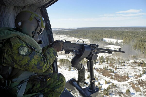 A soldier with a machine gun in a plane over a forest