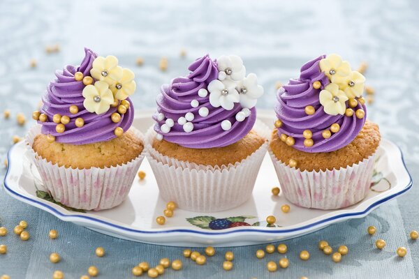 Drei Muffins auf einem Teller mit violetter Creme und Blumen