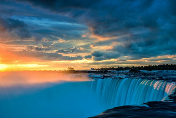 Waterfall landscape with thick clouds on sunset background