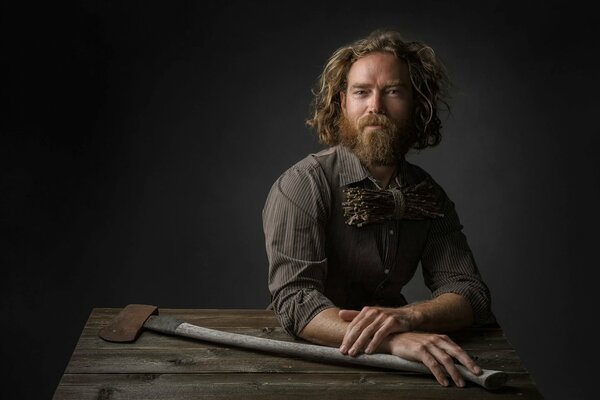 A bearded man in a shirt holds an axe