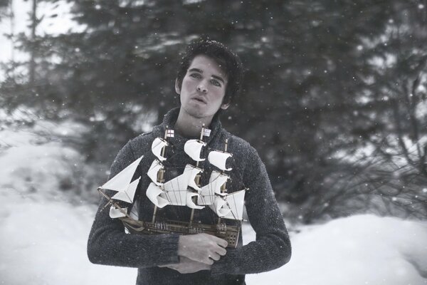 Against the background of snow there is a guy with a boat in his hands