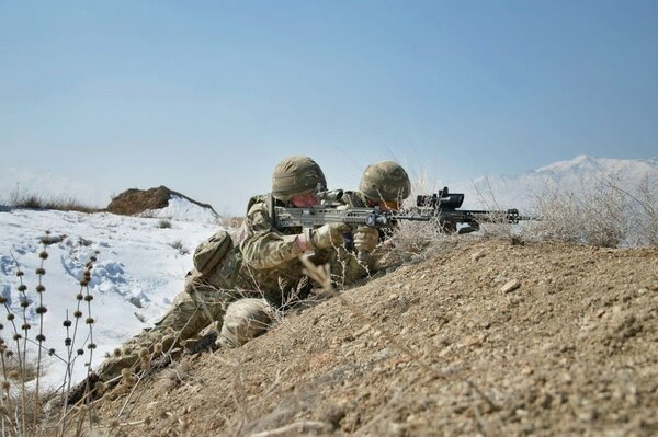 Soldiers with weapons are sitting in a trench