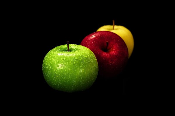 Bodegón tres manzanas de colores sobre un fondo negro