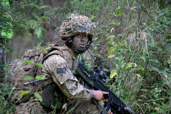 Un soldado con armas de fuego se cuela a través de un bosque salvaje