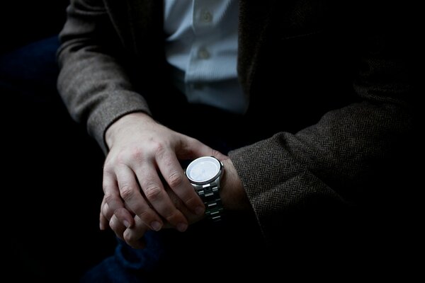 A man in a jacket looks at his wristwatch, determines the time