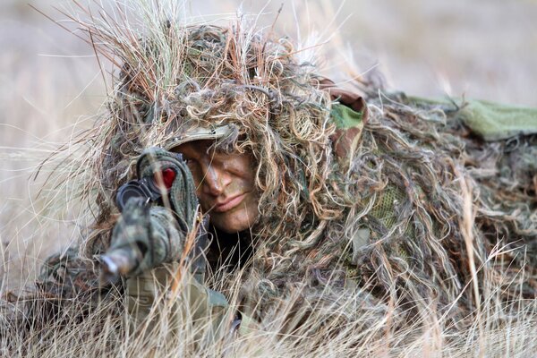 Der Scharfschütze ist mit Gras verkleidet und zielt auf ein Gewehr